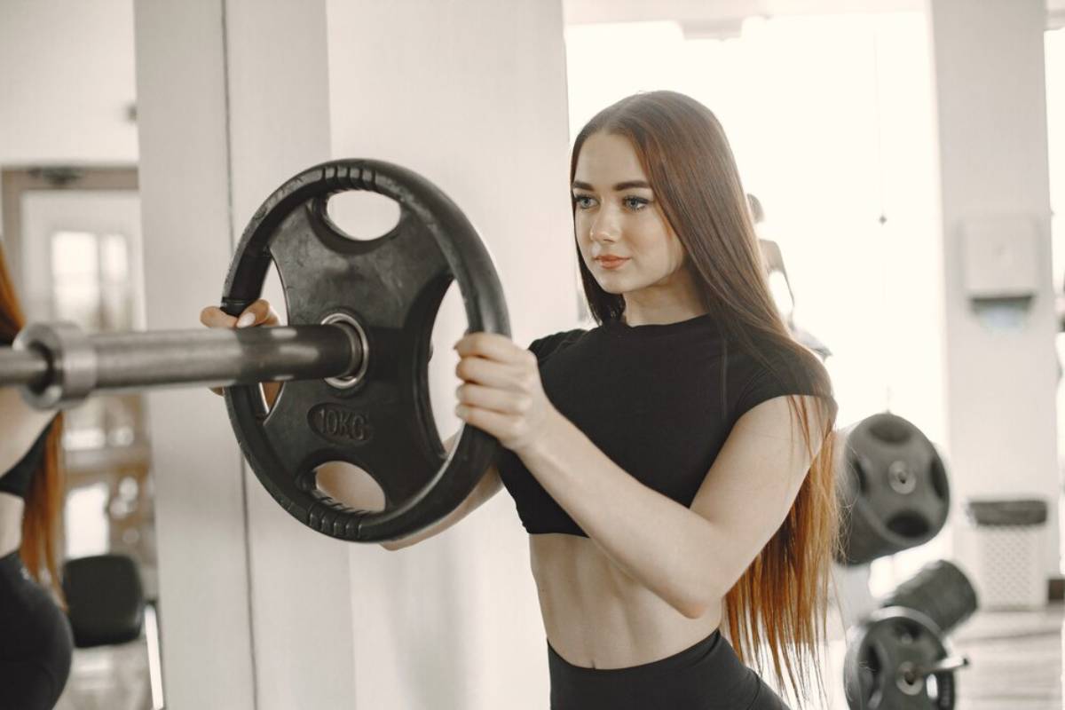 Young woman exercising with a barbell in a gym, focusing intently on her workout.