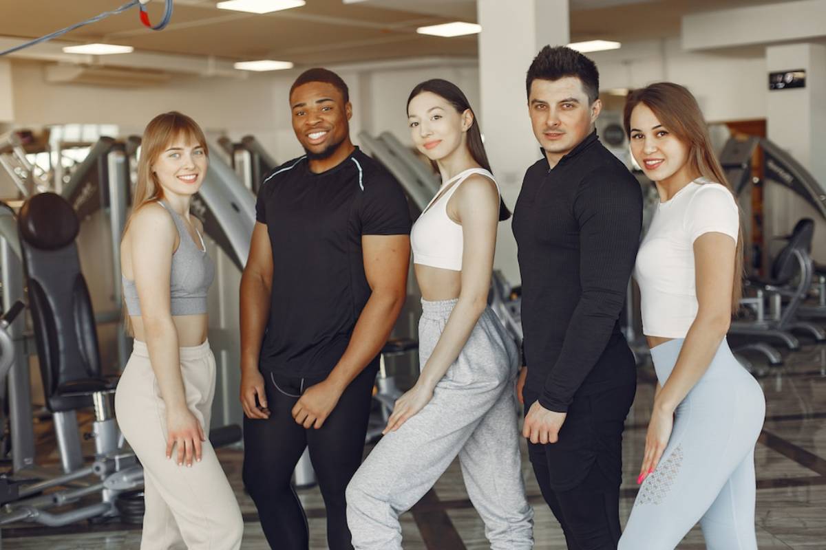 Five diverse young adults posing together in a gym, smiling at the camera.