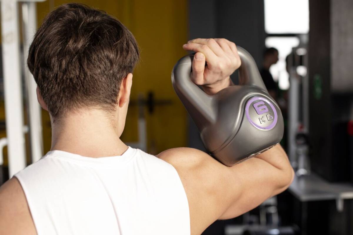A man in a sleeveless shirt lifts a 6 kg kettlebell overhead