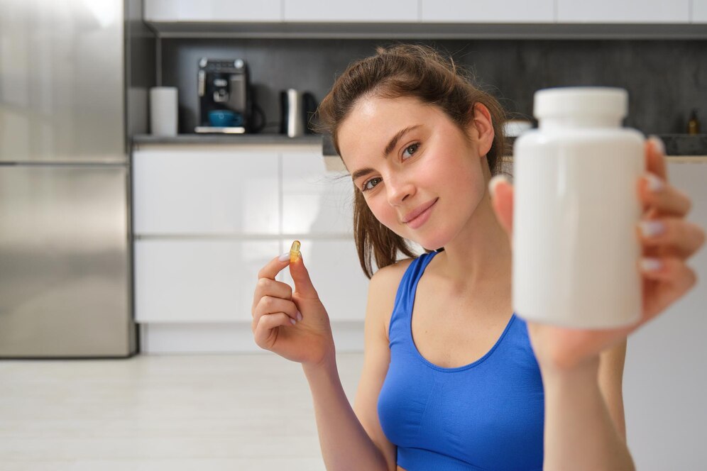 A person in a blue tank top holds a supplement capsule