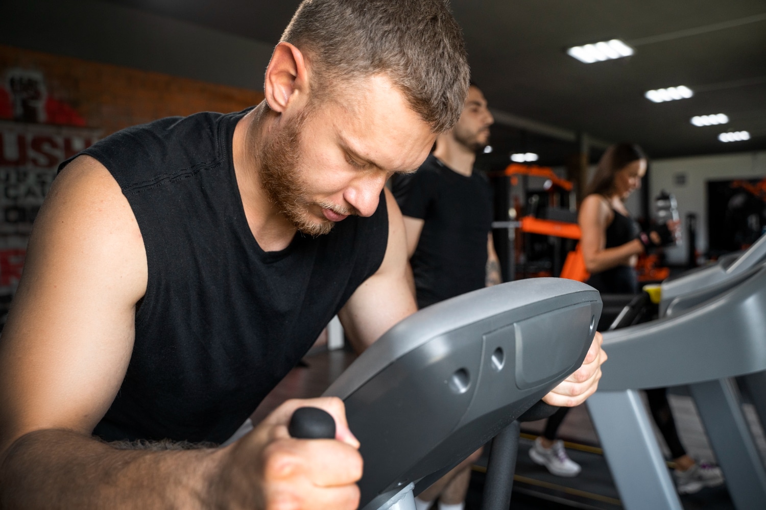 A man exercises intensely on a treadmill in a modern gym, with bright lighting