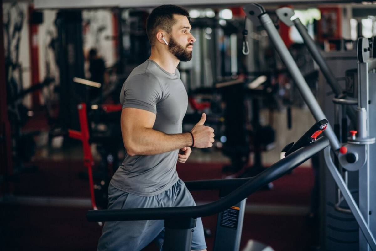 Man jogging on a treadmill in a well-equipped gym, focused and wearing headphones.