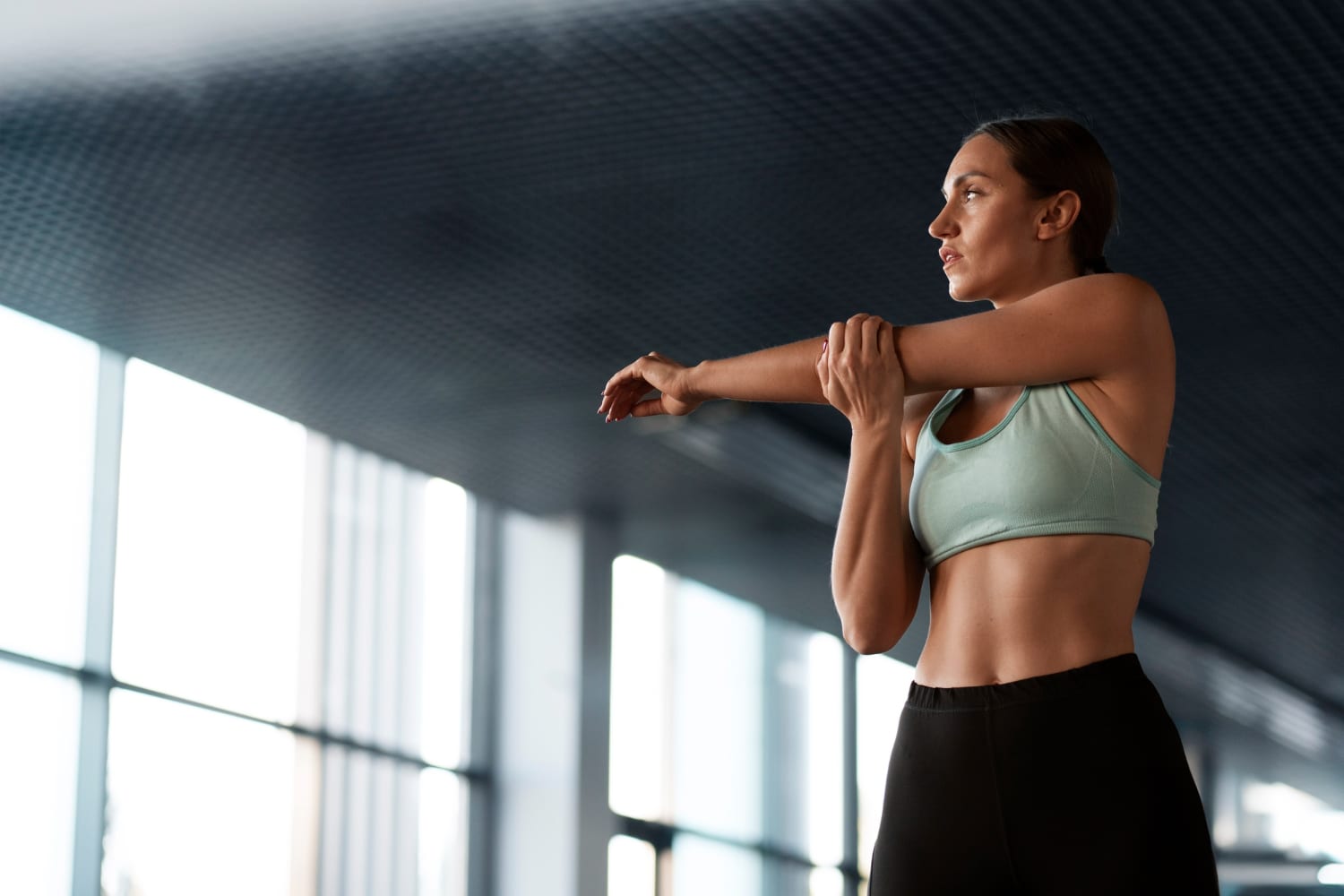 A fit woman stretches her arms in a bright gym, showcasing her toned physique and athletic wear