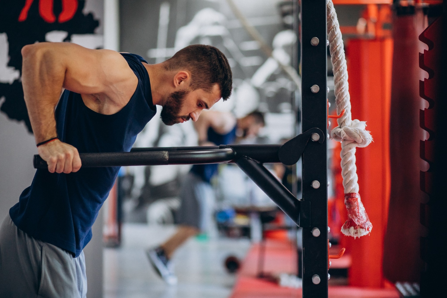 Man performing a dip exercise at a gym with other athletes in the background.