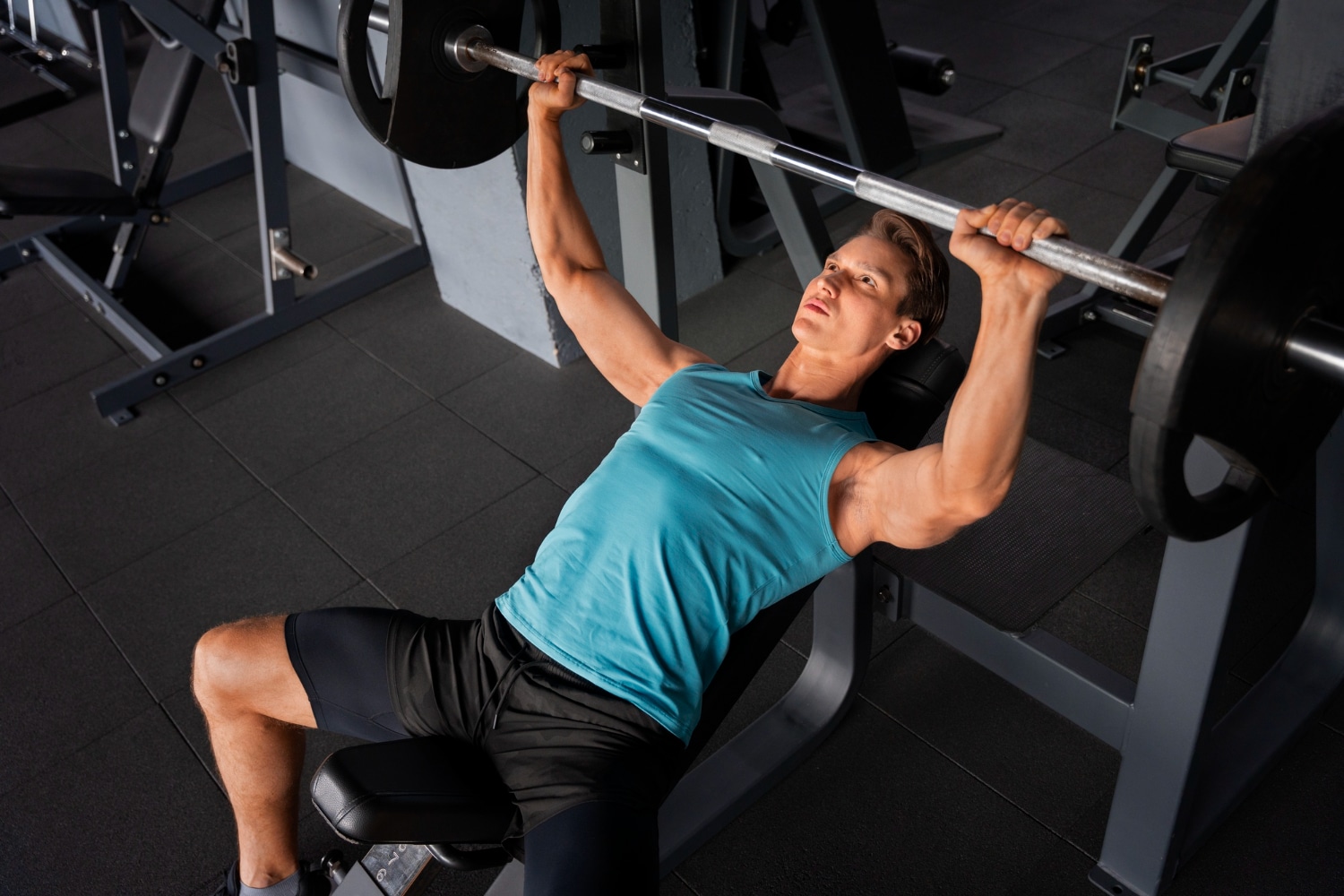 A young man bench pressing weights in a gym.