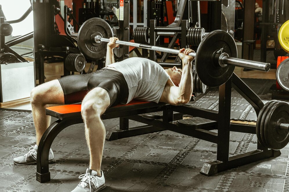 Man lifting weights on a bench press at a gym, surrounded by exercise equipment.