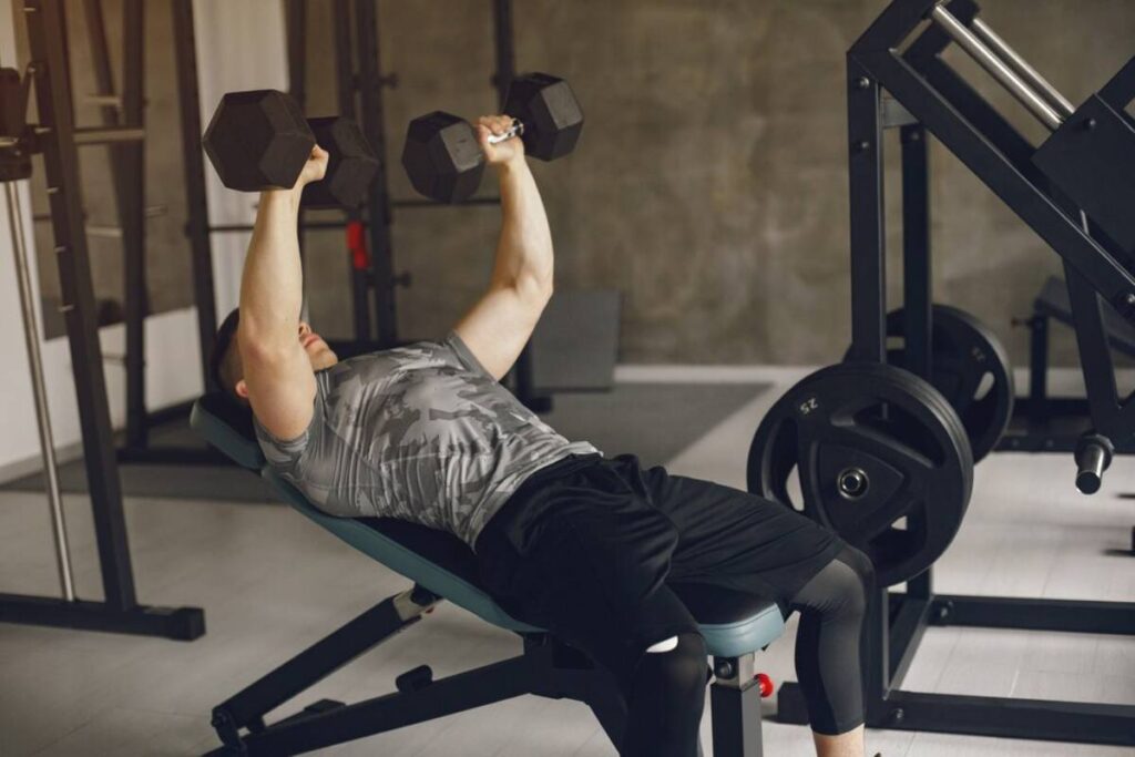 Man lifting heavy dumbbells while lying on an incline bench in a gym.