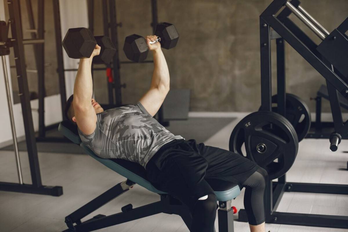 Man lifting heavy dumbbells while lying on an incline bench in a gym.