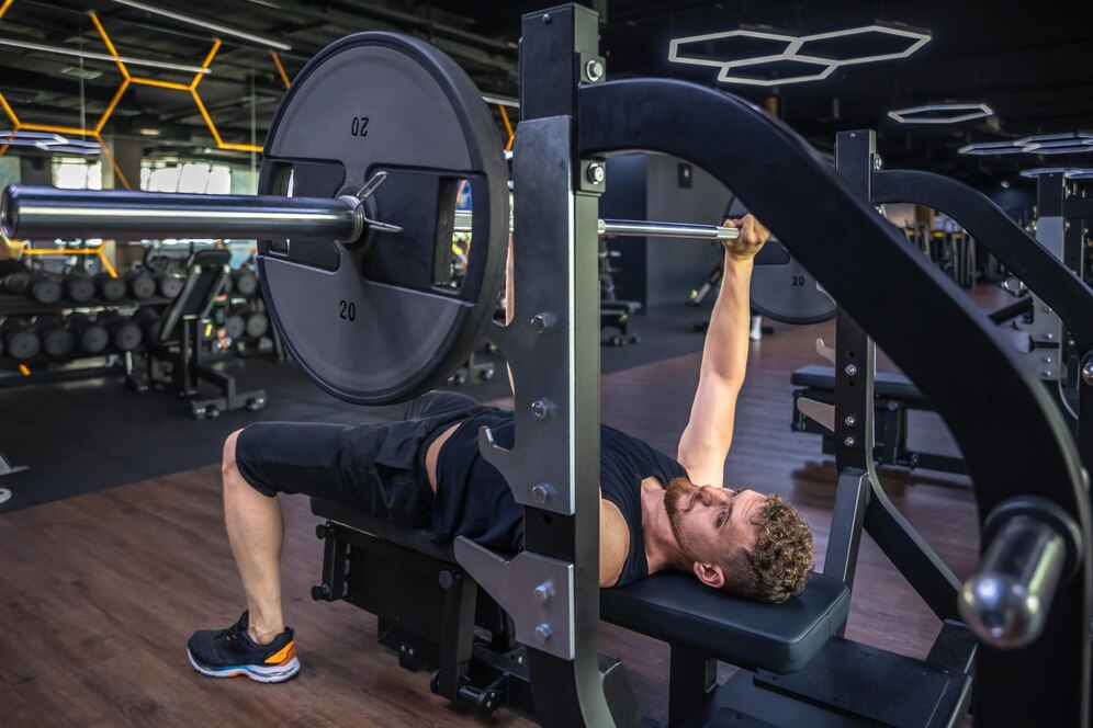 Man lifting weights on a bench press machine at a gym.