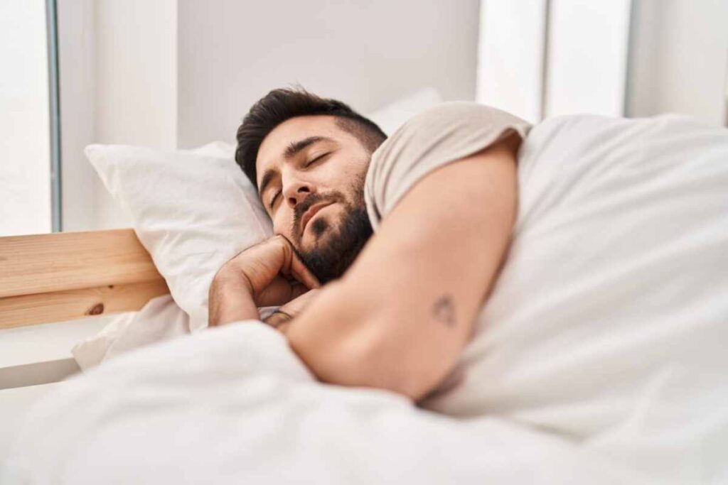 Young man peacefully sleeping on white pillows in a light-filled bedroom.