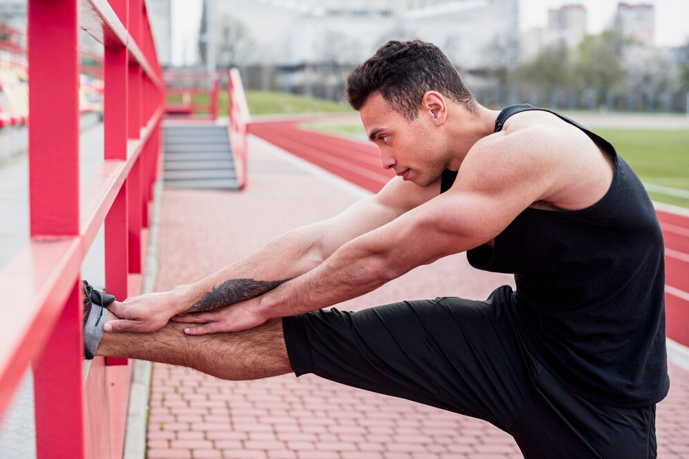 A man stretching his leg on a red railing at an outdoor track field.