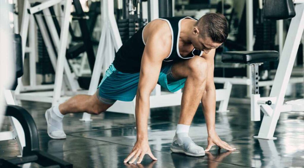 Young man stretching in a gym, focusing on his leg muscles.